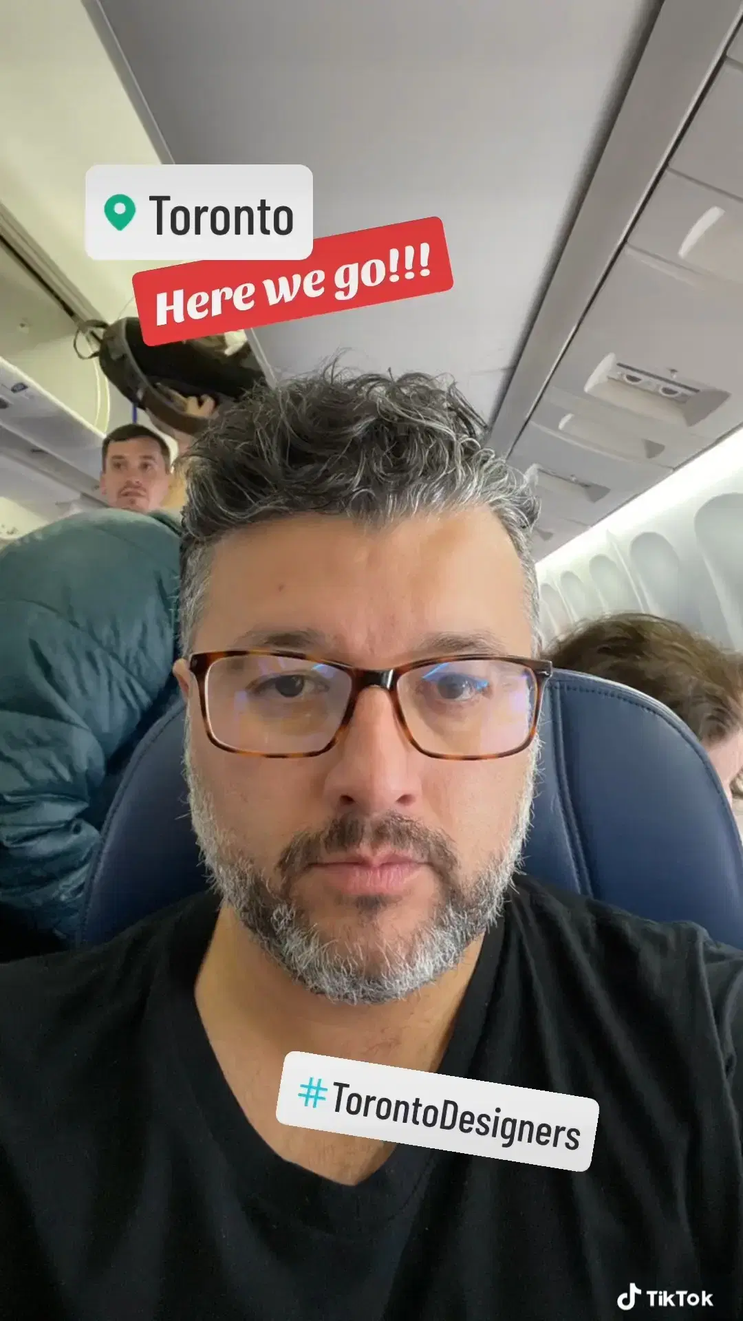 Andrei seated in an airplane wearing a black t-shirt and glasses